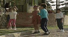 a group of children are playing on a sidewalk in front of a brick building