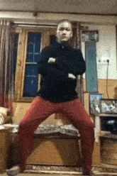 a man in a black shirt and red pants is standing on his knees in a living room .