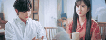 a man and a woman are sitting next to each other at a table with cups of coffee .
