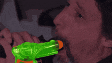 a man is holding a green and orange water gun in his mouth