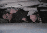 two men looking underneath a car with one wearing a hat