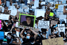 a crowd of people holding signs including one that says " black lives matter "