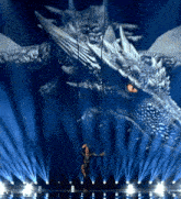 a woman stands on a stage with a large dragon behind her