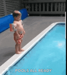 a baby is standing on the edge of a swimming pool wearing life preservers .