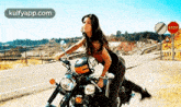 a woman is riding a motorcycle on the side of a road with a stop sign in the background
