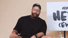 a man with a beard sits in front of a sign that says he 's crew