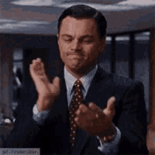 a man in a suit and tie is clapping his hands while making a face .