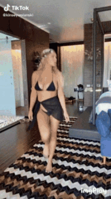 a woman in a bikini and skirt is walking on a rug in a room .