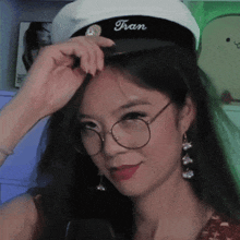 a woman wearing glasses and a hat with tran embroidered on it