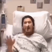 a man in a hospital bed is smoking a cigarette and making a funny face .