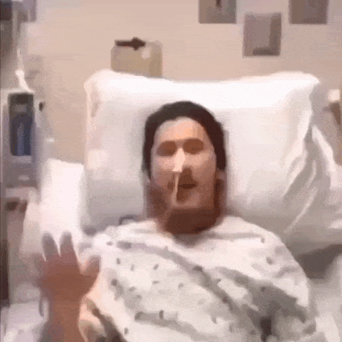 a man in a hospital bed is smoking a cigarette and making a funny face .