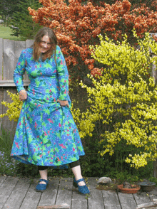 a woman in a blue and green dress is standing on a wooden deck