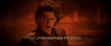 a man in a black suit is standing in a dark room with a red background and says `` you underestimate my power '' .