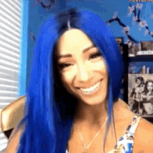 a woman with blue hair is smiling and looking at the camera in a room .