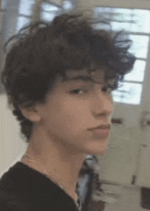 a young man with curly hair is wearing a black shirt and necklace .