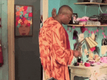 a man in an orange robe is standing in a room with a painting on the wall
