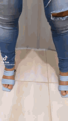 a woman wearing a pair of light blue heels and ripped jeans is standing on a tiled floor .