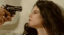 a woman is laying on a bed while a man is pointing a gun at her face .