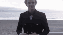 a man in a suit and bow tie stands on a beach