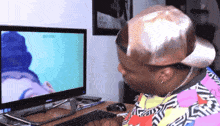 a man wearing a hat looks at a computer monitor