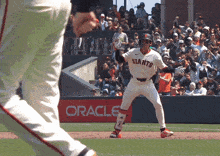 a baseball player wearing a giants jersey stands in front of an oracle sign