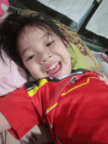 a little girl wearing a red shirt with a yellow stripe on the sleeves is smiling