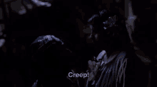 a woman is holding a man 's head in a dark room and says creep .