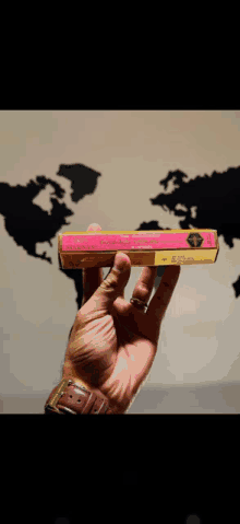 a hand is holding a pink box with a yellow label