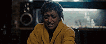 a woman wearing a yellow robe is crying in a dark room