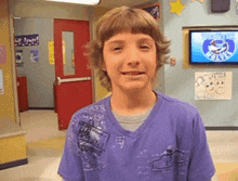 a young boy wearing a purple shirt is smiling in front of a tv that says ' shark tank ' on it