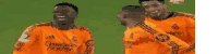 two men in orange jerseys are standing next to each other on a green field .