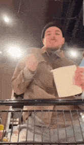 a man in a hat is holding a piece of paper in his hand while standing in a shopping cart .