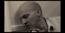 a bald man is leaning against a wall while holding a napkin