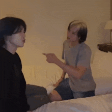 two men are sitting on a bed talking to each other and one of them is pointing at the other .