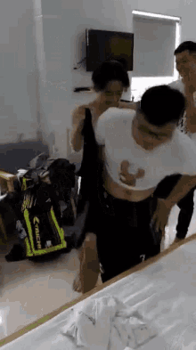 a group of people are standing around a man in a white shirt and black shorts in a room .