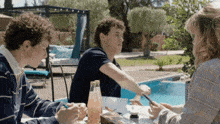 three people are sitting at a table by a pool