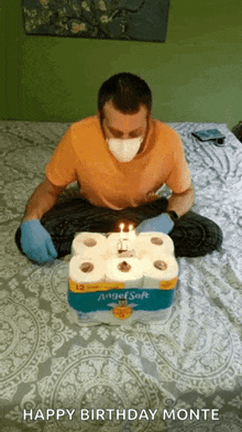 a man wearing a mask and gloves is sitting on a bed with a birthday cake made out of toilet paper .