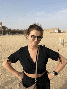 a woman wearing glasses and a black top is standing on a beach