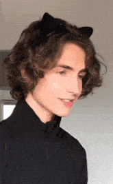 a young man with curly hair is wearing a black jacket and a black headband with cat ears