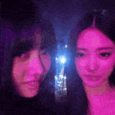two women are posing for a picture in a dark room with purple lights behind them .