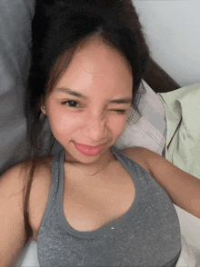 a woman in a grey tank top is laying on a bed