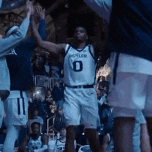 a basketball player wearing a butler jersey is giving a high five to his teammates