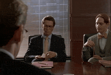 a man in a suit and tie is sitting at a table with two other men