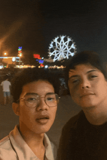 two young men pose for a picture in front of a ferris wheel at night