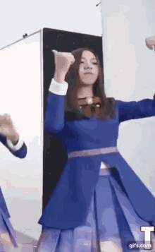 a woman in a blue dress is dancing in front of a white board .