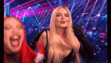 a blonde woman is standing next to a red haired woman on a stage in front of a crowd .