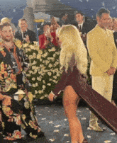 a group of people are standing around a woman in a high slit dress