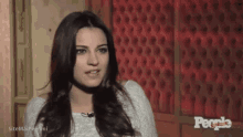 a woman is talking to a microphone in front of a red wall with people written on it
