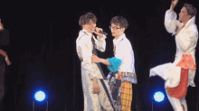 two men are standing next to each other on a stage and one of them is holding a microphone .