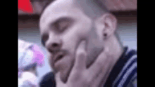 a man with a beard is touching his face with his hand .